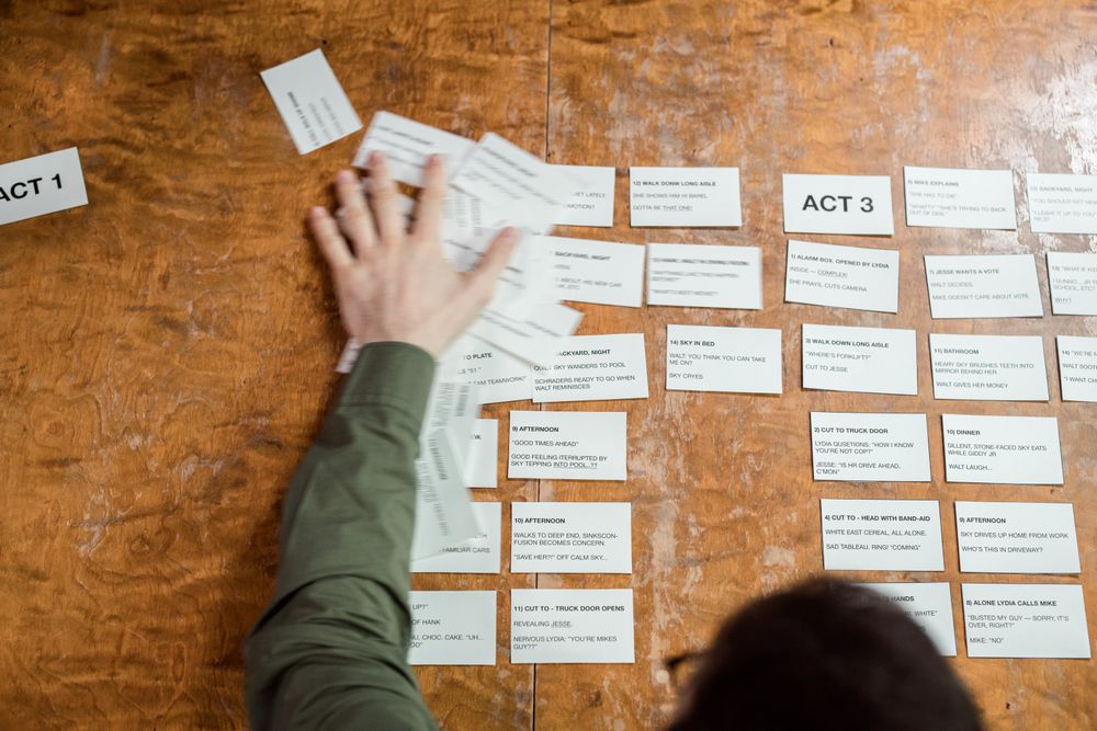 A writer arranging story cards across a wooden table